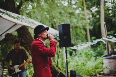 Bräutigam in rotem Anzug und Hut singt.