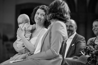 Bride holding a baby looking at her wife in church.