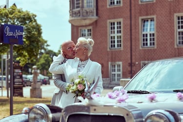 Groom hugging bride from behind next to a car.
