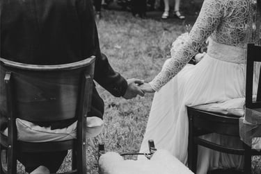 Bride and groom holding hands while sitting on chairs.