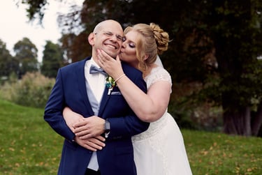 Bride hugging the groom from behind and kissing his cheeks.