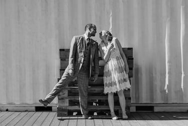 Bride and groom looking at each other in front of palettes and metal container.
