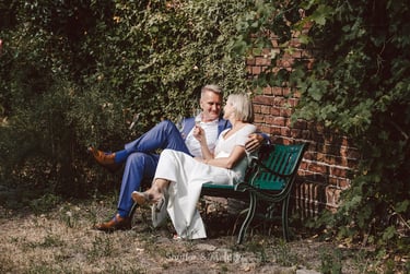 A mature bride and groom sitting on a bench toasting each other.