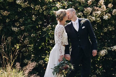Bride and groom kissing in a garden in front of a large hedge.