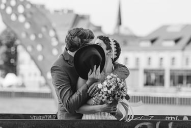 Groom covering his and bride's face with a hat while they kiss.