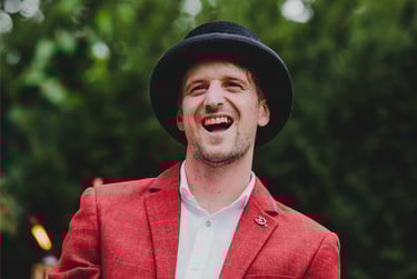 Groom in a red suit and hat laughing.