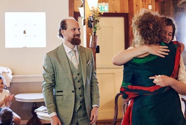 Groom looking at his mother in law hugging the bride.