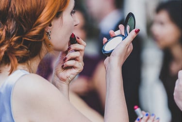 Eine Hochzeitsgast, die in ihren Spiegel schaut und ihren roten Lippenstift nachzieht.