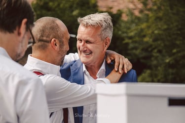 A smiling groom being hugged by a wedding guest.