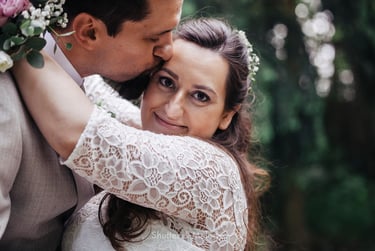 Bride looking into the camera and being kissed on her temple by the groom.