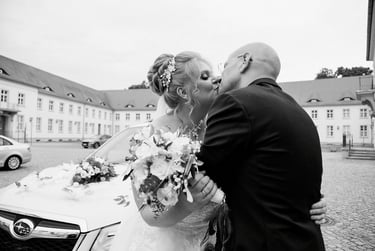 Bride and groom kissing in front of a car.
