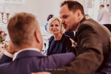 Die Mutter der Braut schaut in die Kamera, während die Hochzeitsgäste sich unterhalten.