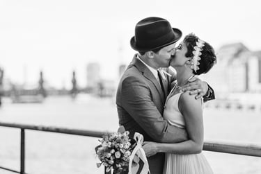 Frischvermählte küssen sich am Flussufer mit der Oberbaumbrücke im Hintergrund.