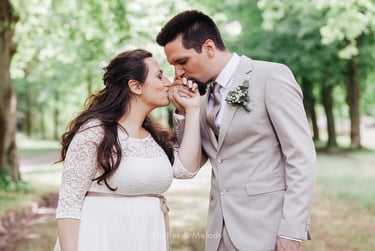 Bride and groom kissing each other's hands in a park.