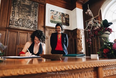 Bride signing the marriage documents while her wife is looking over her shoulder.