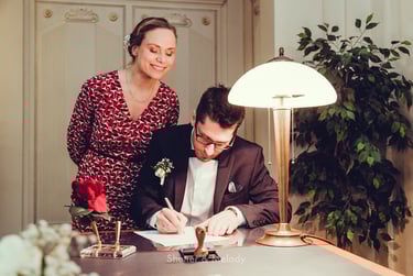 Groom signing marriage documents while bride is looking over his shoulder.
