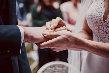 Bride putting on wedding band on husband's finger.