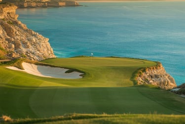 Luxury oceanside golf course green on a cliff overlooking the turquoise sea at sunset.