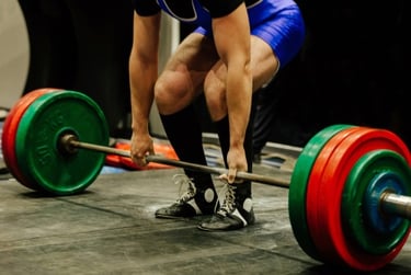 A powerlifter in a blue singlet performing a heavy barbell deadlift with colored plates at a competition.