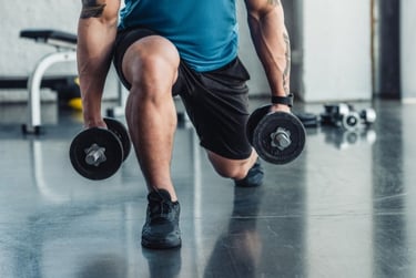 Muscular man performing weighted lunges with dumbbells during a leg workout at the gym.