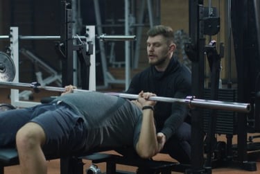 A personal trainer spotting a man performing a barbell bench press during a gym workout.