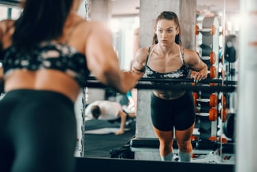 A focused athletic woman performs strength training exercises in front of a gym mirror.
