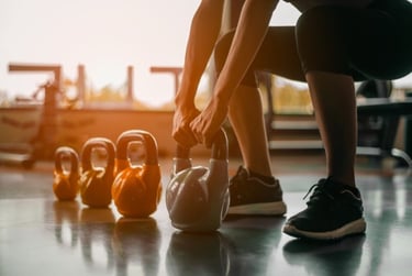 A woman performing a kettlebell squat at the gym with a row of weights on the floor.
