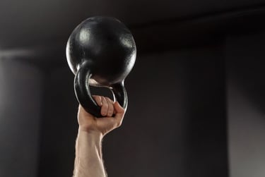 A person lifting a heavy black cast iron kettlebell overhead for strength training in a gym.