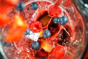 Fresh blueberries and raspberries splashing into a red berry fruit smoothie inside a glass blender.