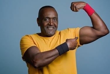 Fit senior Black man in a yellow t-shirt flexing bicep muscles showing strength and health.