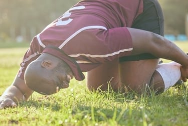 Injured rugby player holding his ankle in pain on a grass field during a sports match.