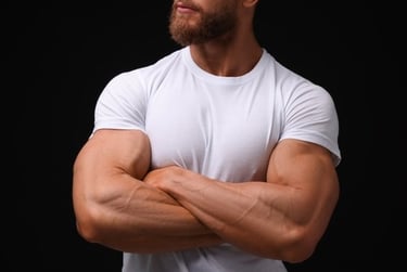 Muscular man with a beard wearing a white t-shirt and crossing his arms against a black background.