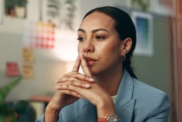 A pensive female professional in a blue blazer brainstorming at her creative office desk.