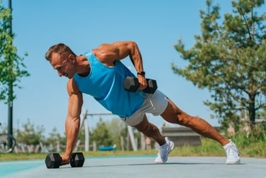 Muscular man performing a dumbbell renegade row plank exercise outdoors for core and strength training.
