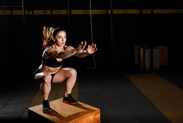 Athletic woman performing a box jump exercise for plyometric training in a dark gym setting.