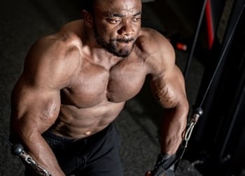 Muscular man performing a cable chest fly workout for bodybuilding strength training in a dark gym.