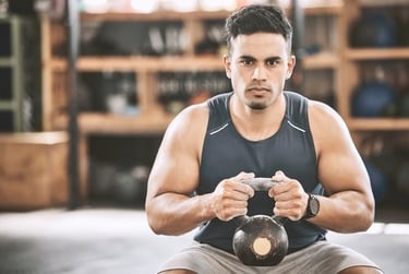 A muscular man holding a kettlebell during a strength training workout at a gym.