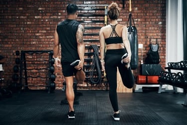 A man and woman stretching their quads during a workout in a rustic industrial gym.