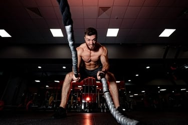 Muscular man doing high-intensity battle rope workout for core strength in a dark gym setting.