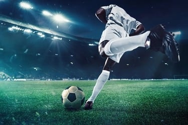 Professional soccer player kicking a ball on a grass field in a stadium under bright lights.