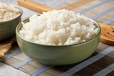 A green ceramic bowl filled with fluffy cooked white jasmine rice on a bamboo mat.