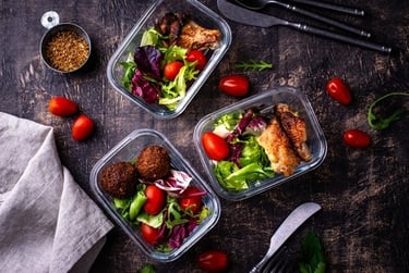 Glass meal prep containers with healthy salads, roasted chicken, and falafel on a dark wooden table.