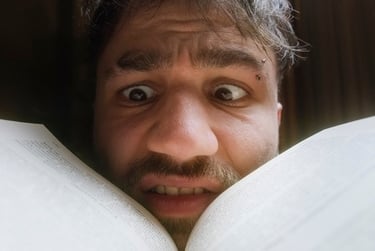 A man with a shocked expression reads a book with wide eyes and a look of surprise.