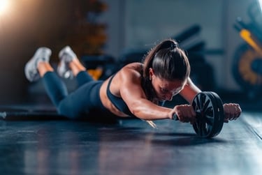 A woman performing a core workout using an ab roller wheel for abdominal strength training in a gym.