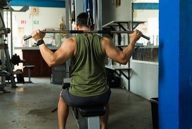 A muscular man performing lat pulldowns on a cable machine for back strength training in a gym.