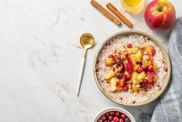 Healthy oatmeal bowl with cooked apples, cinnamon sticks, and fresh cranberries on a marble background.