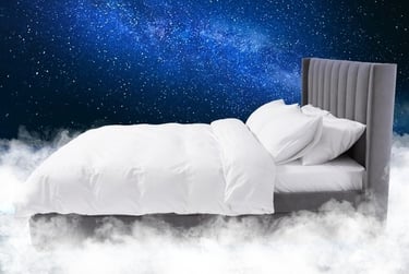 A modern grey upholstered bed with white bedding floating in white clouds under a starry blue night sky.