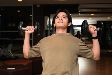 A young man performing a seated dumbbell shoulder press exercise at a gym.