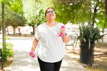 Plus-size woman in white t-shirt power walking outdoors with pink dumbbells for fitness.