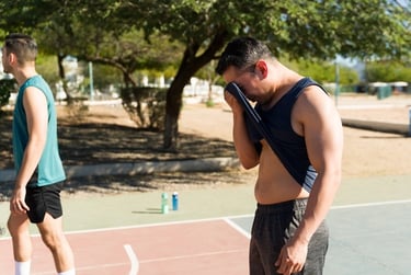 Sweaty man wiping forehead with his tank top after outdoor sports workout on a basketball court.